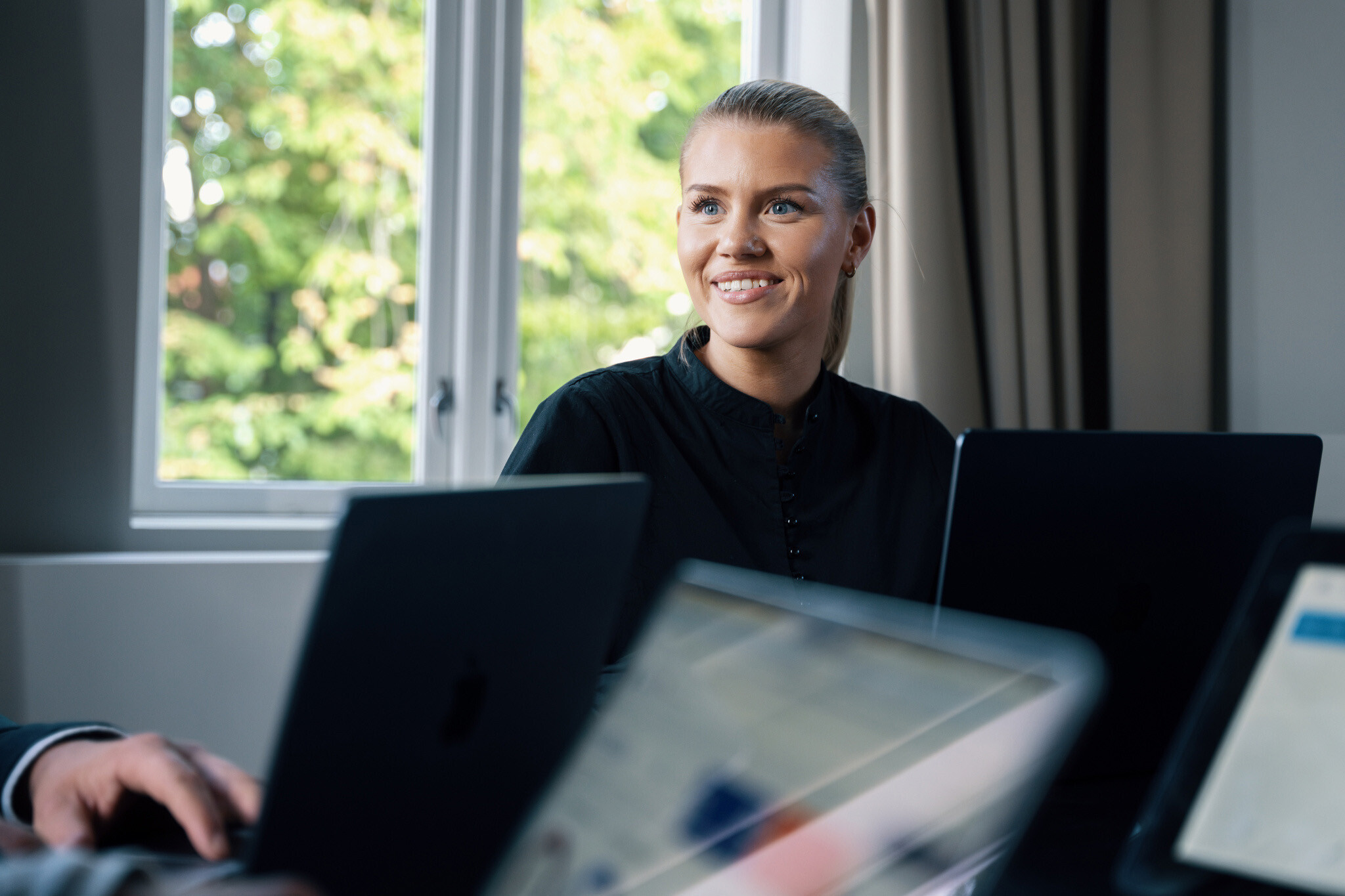 Kvinne sitter rundt et bord med laptoper på og smiler mens hun ser til venstre